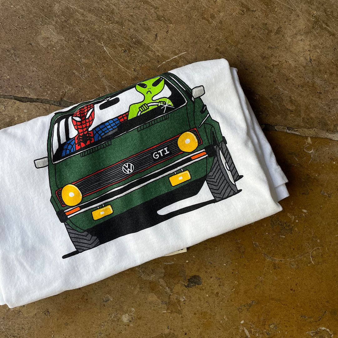 Folded view of the Unisex Ring-Spun Cotton Crewneck Heavyweight T-Shirt in white, depicting Spiderman and a green alien on a road trip in a vintage green Volkswagen Golf
