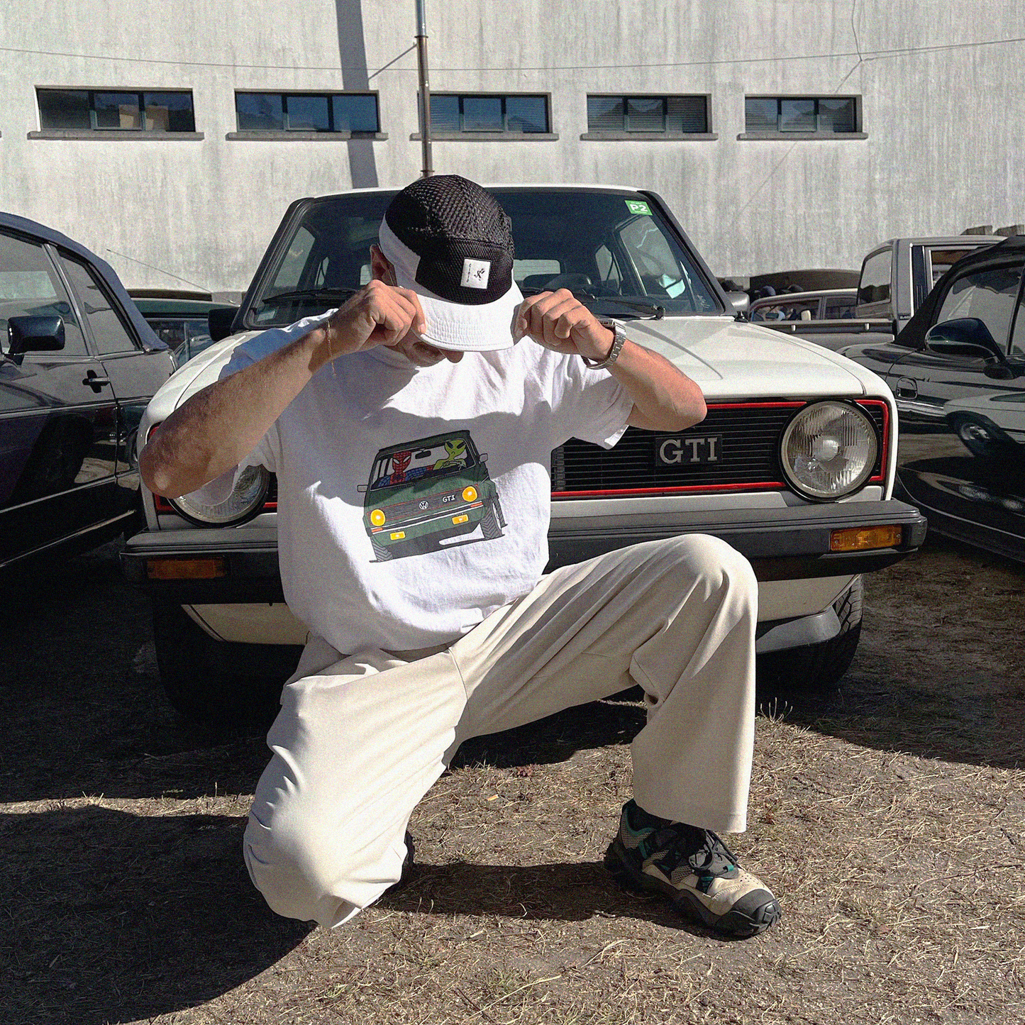 Model wearing the Unisex Ring-Spun Cotton Crewneck Heavyweight T-Shirt in white, depicting Spiderman and a green alien on a road trip in a vintage green Volkswagen Golf. A vw Golf MK1 on the back