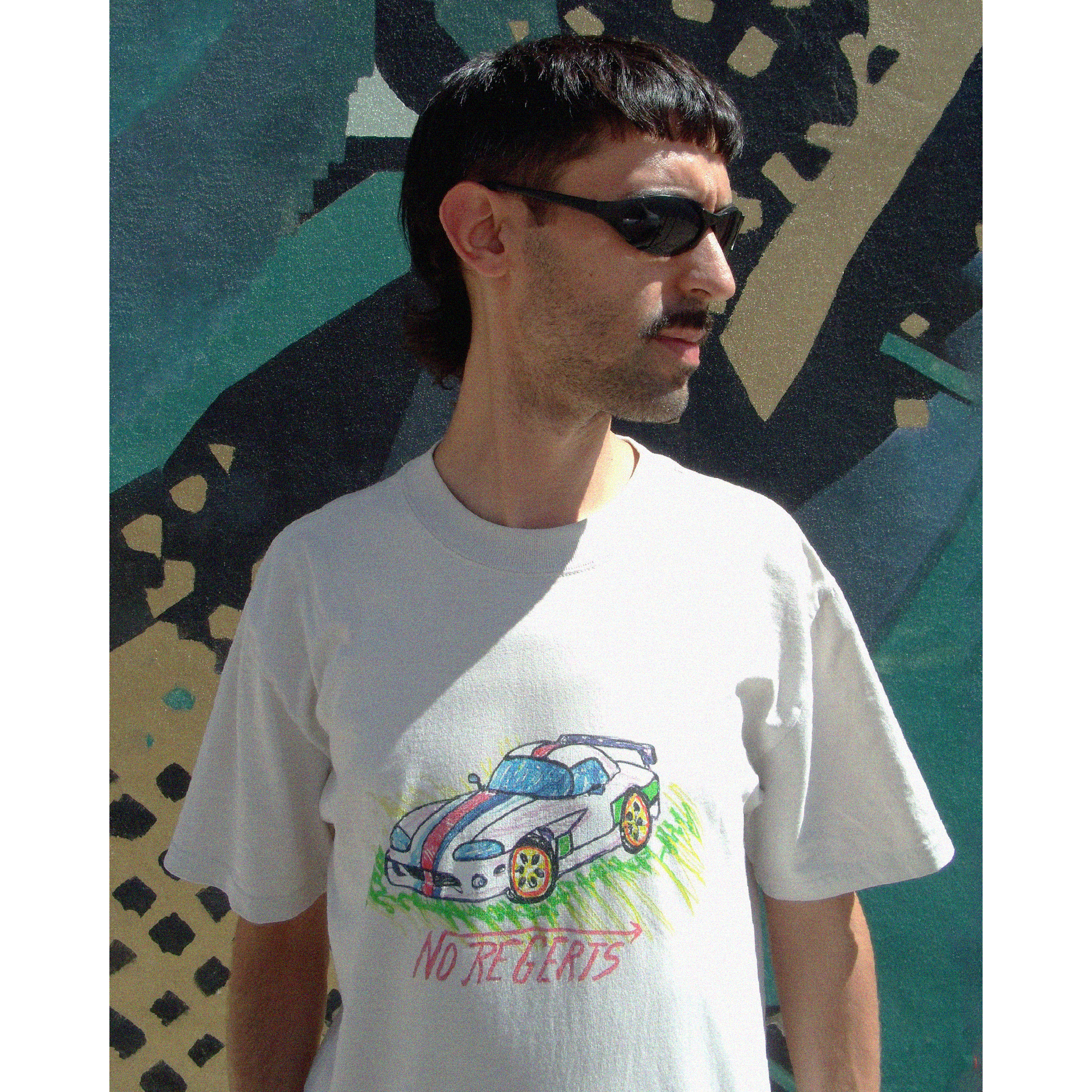 Model wearing the Oversize fit unisex t-shirt in Bone Color - with naive crayon style Dodge Viper bootleg print in childlike drawing and a tag-style writing saying "No Regerts", in front of a wall